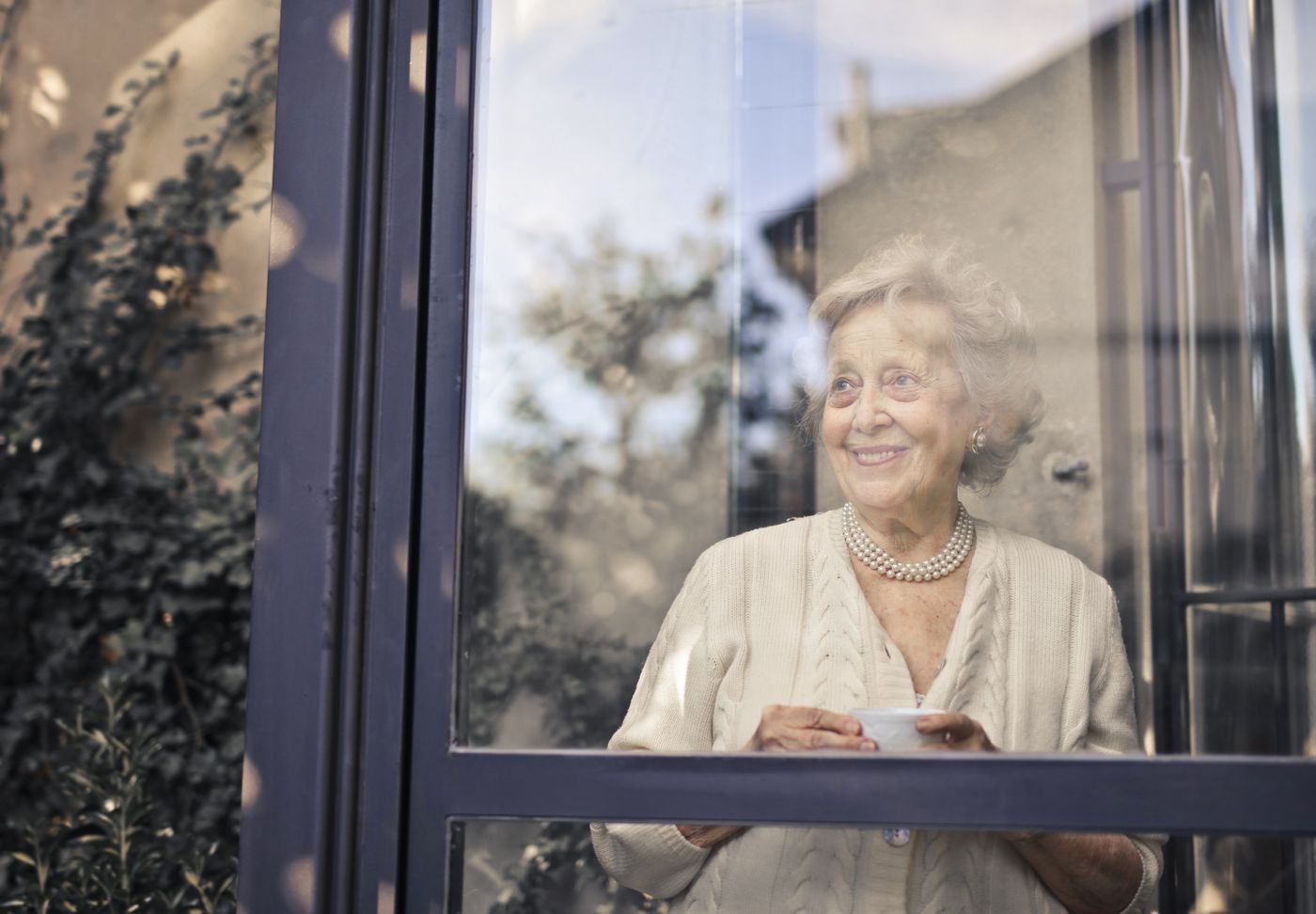 A smiling senior woman holding a cup of tea by a sunny window at home